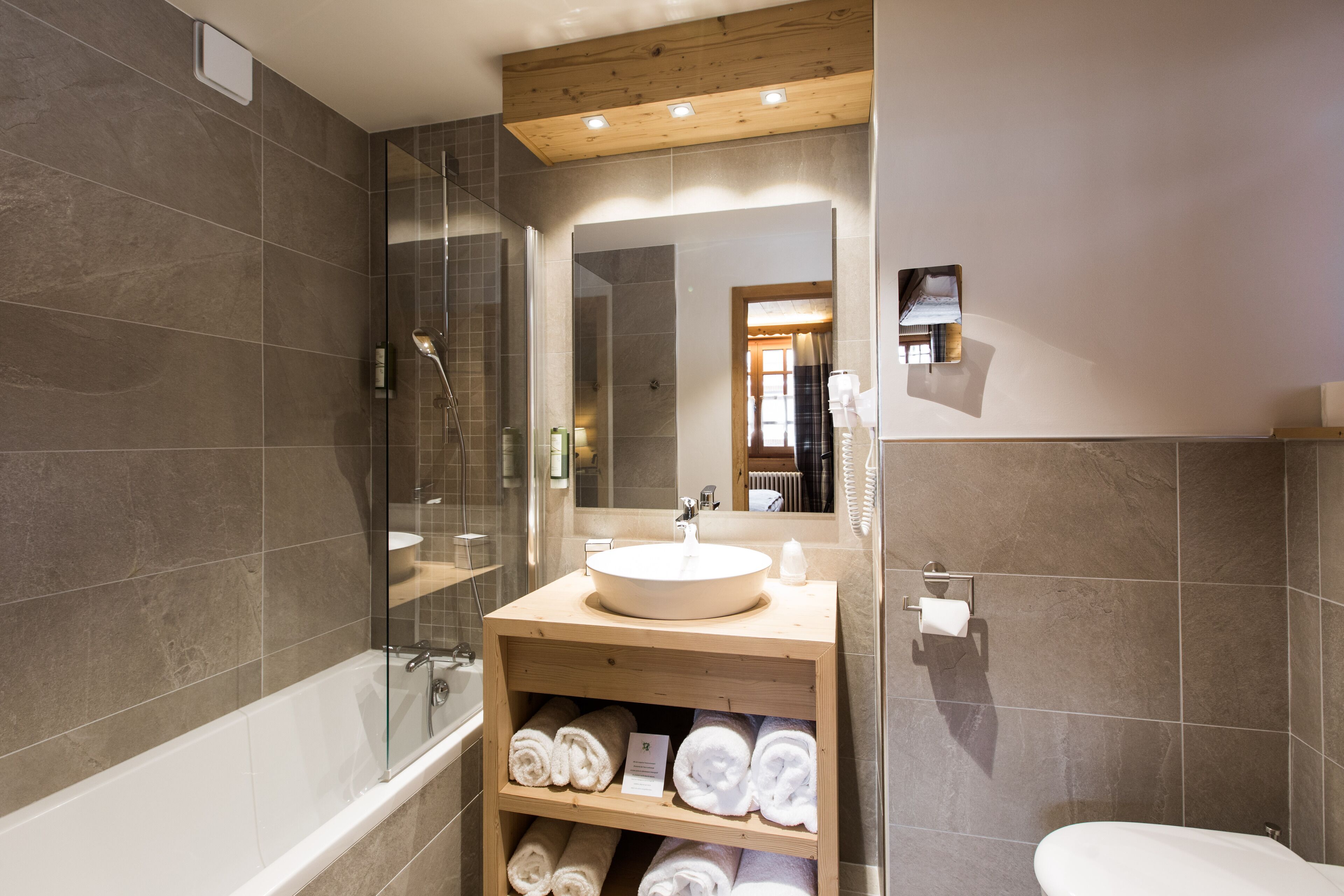 A modern bathroom with a bathtub, a glass-enclosed shower, a wooden vanity with a sink, and a toilet.