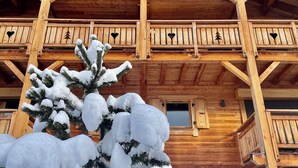 A wooden cabin with a stone foundation, multiple balconies, and a snow-covered pine tree in the foreground. - Hôtel La Griyotire (Praz-sur-Arly)