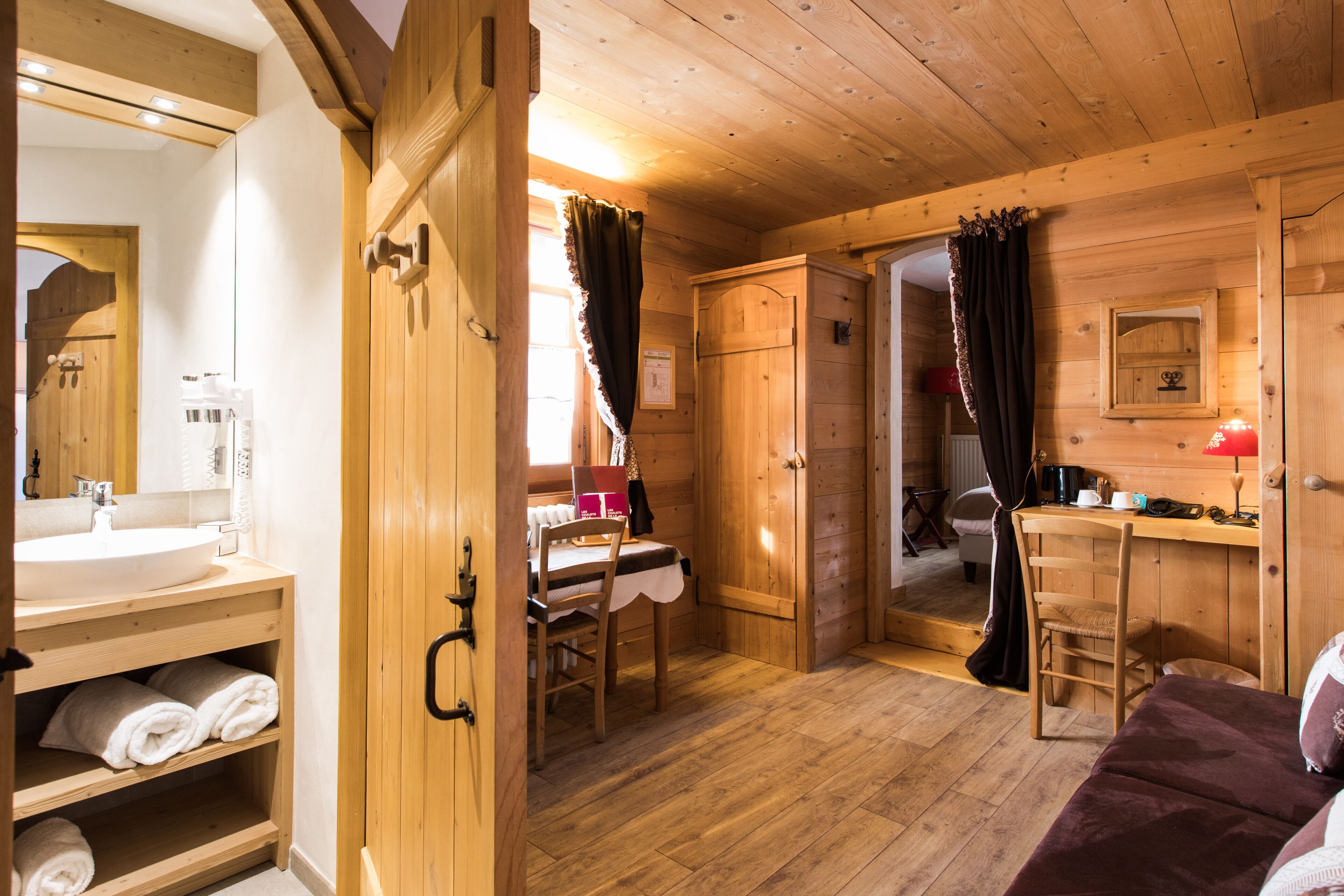 A wooden cabin interior with a bathroom, a dining area, and a bed.