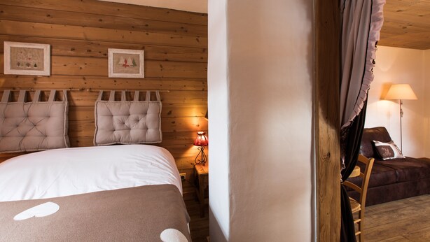 Un dormitorio con techo de madera, una cama con colcha blanca y marrón, una mesita de noche con una lámpara y una silla de madera.