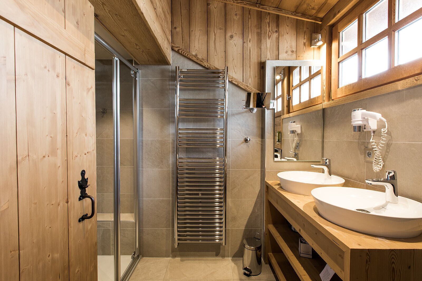 Une salle de bain moderne avec des murs en bois, une cabine de douche en verre, un porte-serviettes et deux vasques avec des robinets.