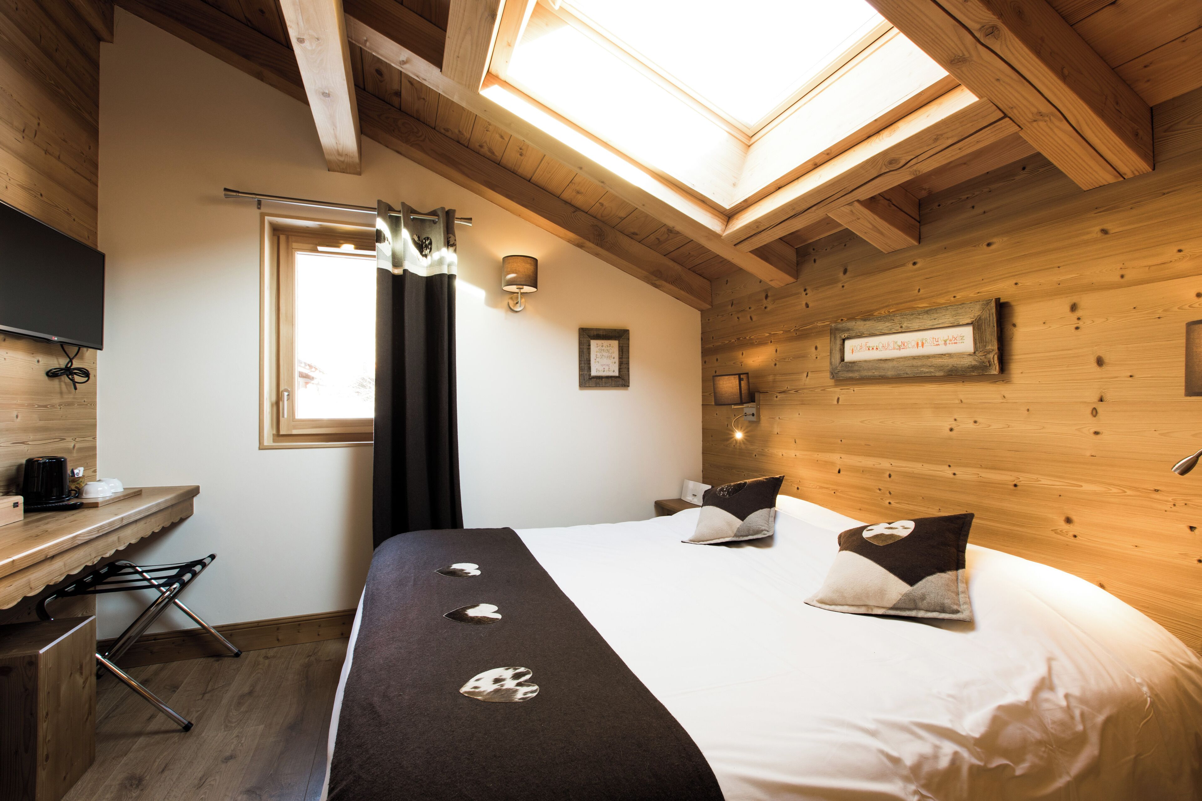 Un dormitorio con tragaluz, una cama con almohadones decorativos, una mesita de noche con lámpara y un panel de pared de madera.