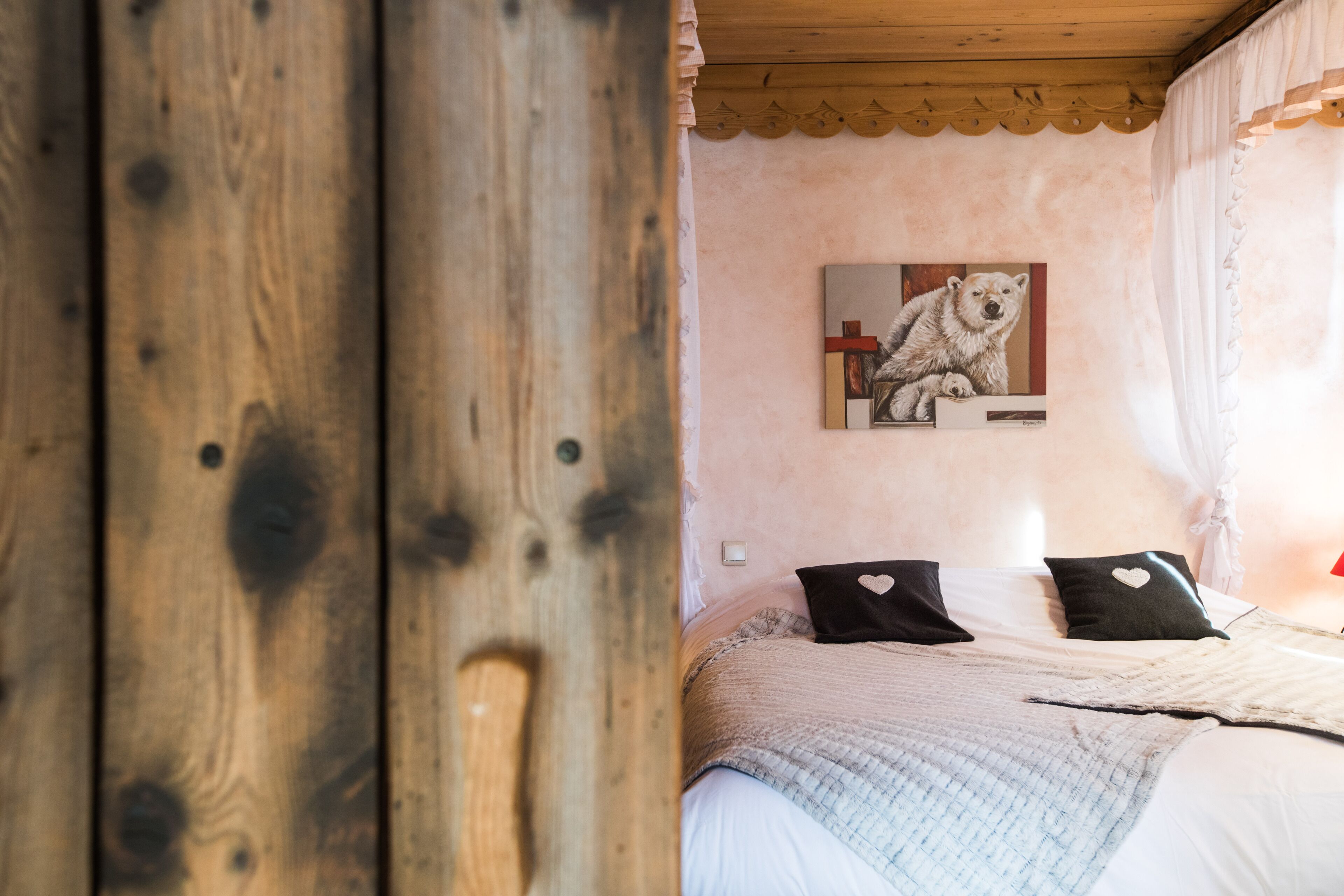 A bedroom with a wooden ceiling, a bed with white bedding, two heart-shaped pillows, and a painting of a polar bear on the wall.