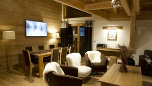 A cozy wooden interior with a dining area, sofas, and a TV mounted on the wall. - Hôtel La Griyotire (Praz-sur-Arly)