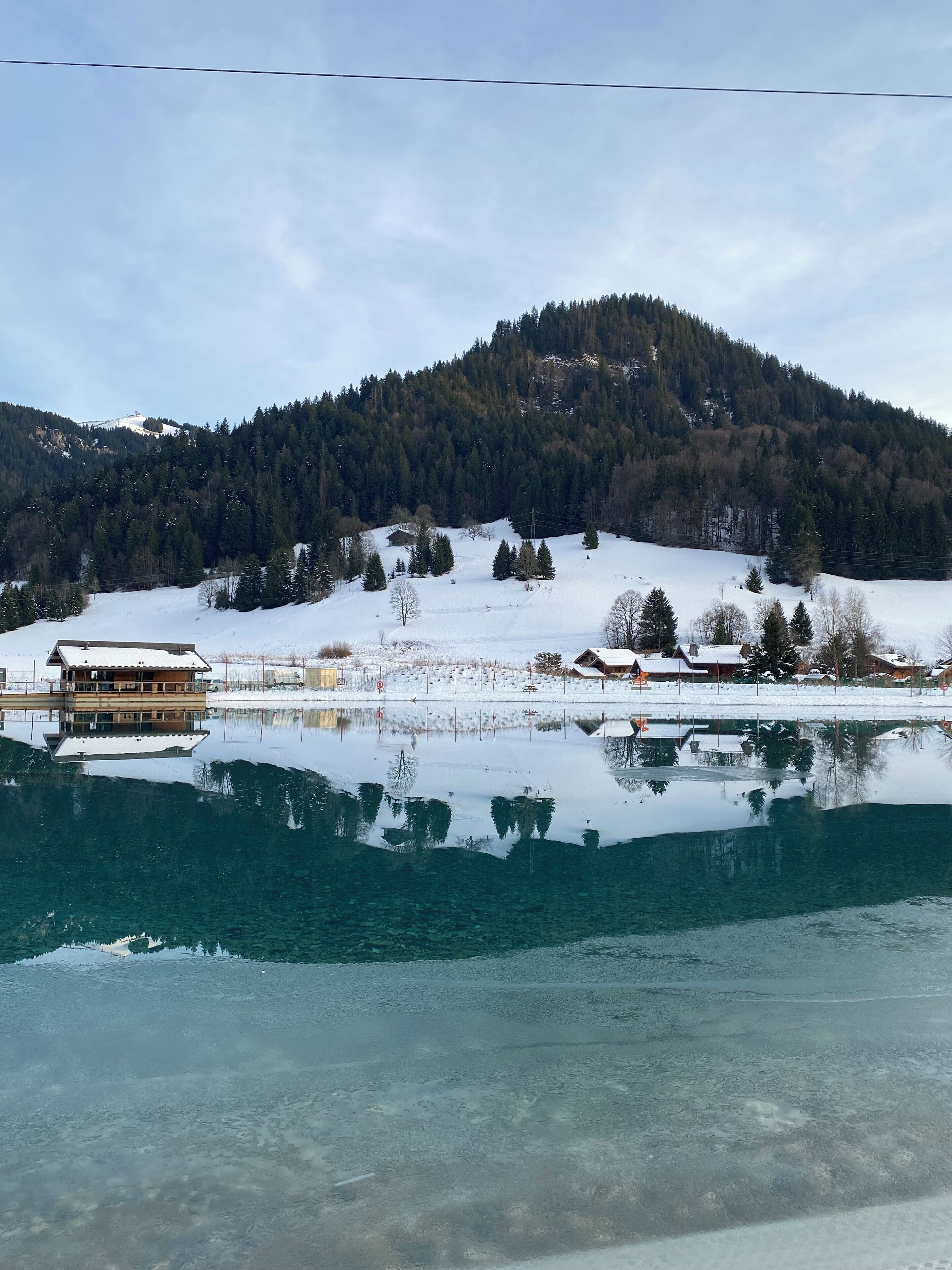 Un lago tranquilo que refleja edificios y una montaña cubierta de bosque.