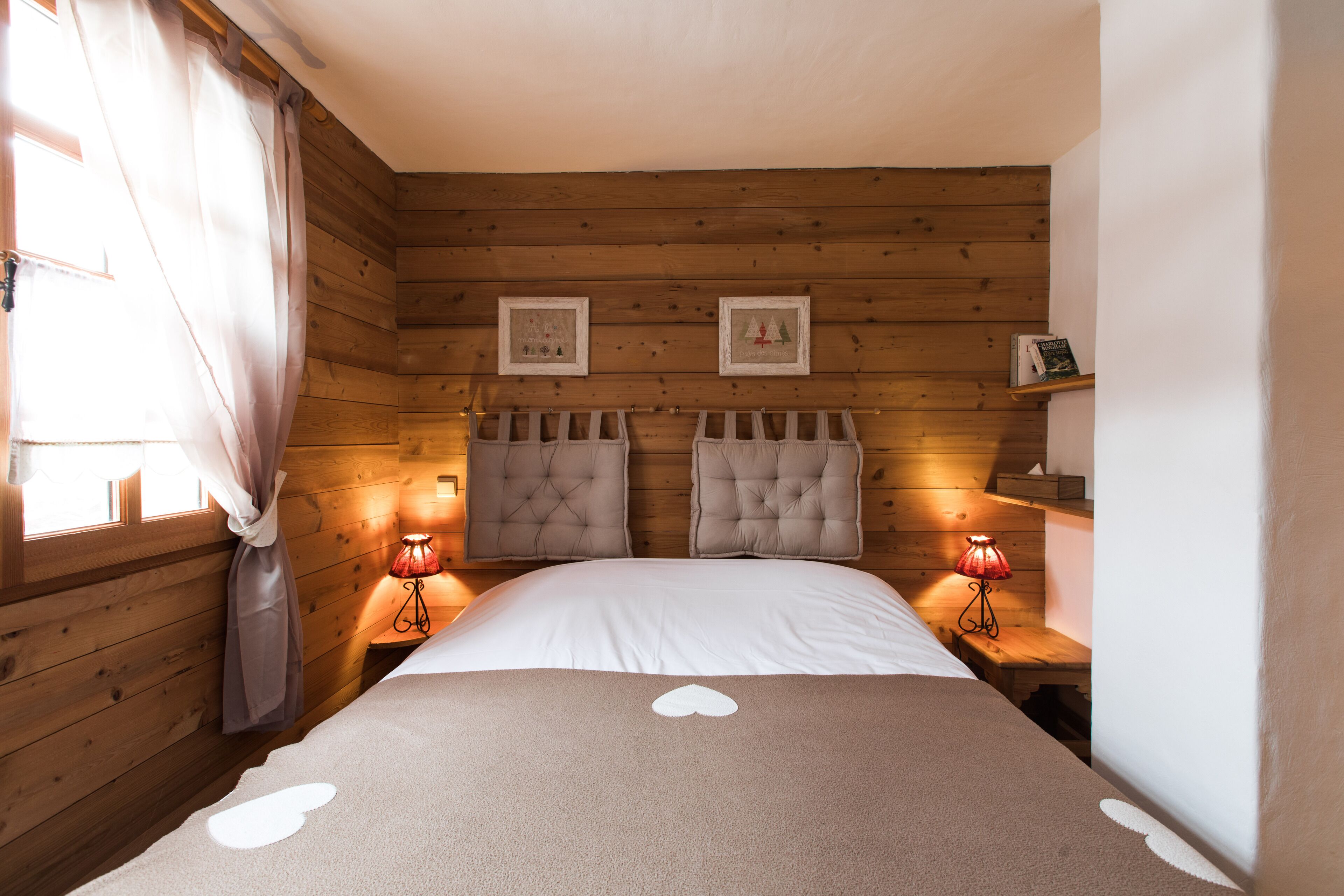 A wooden-paneled bedroom with two beds, each with a tufted headboard, bedside lamps, and framed pictures on the wall.