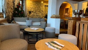 A cozy room with a stone wall, a wooden ceiling, a sofa, a coffee table, and a Christmas tree. - Hôtel La Griyotire (Praz-sur-Arly)