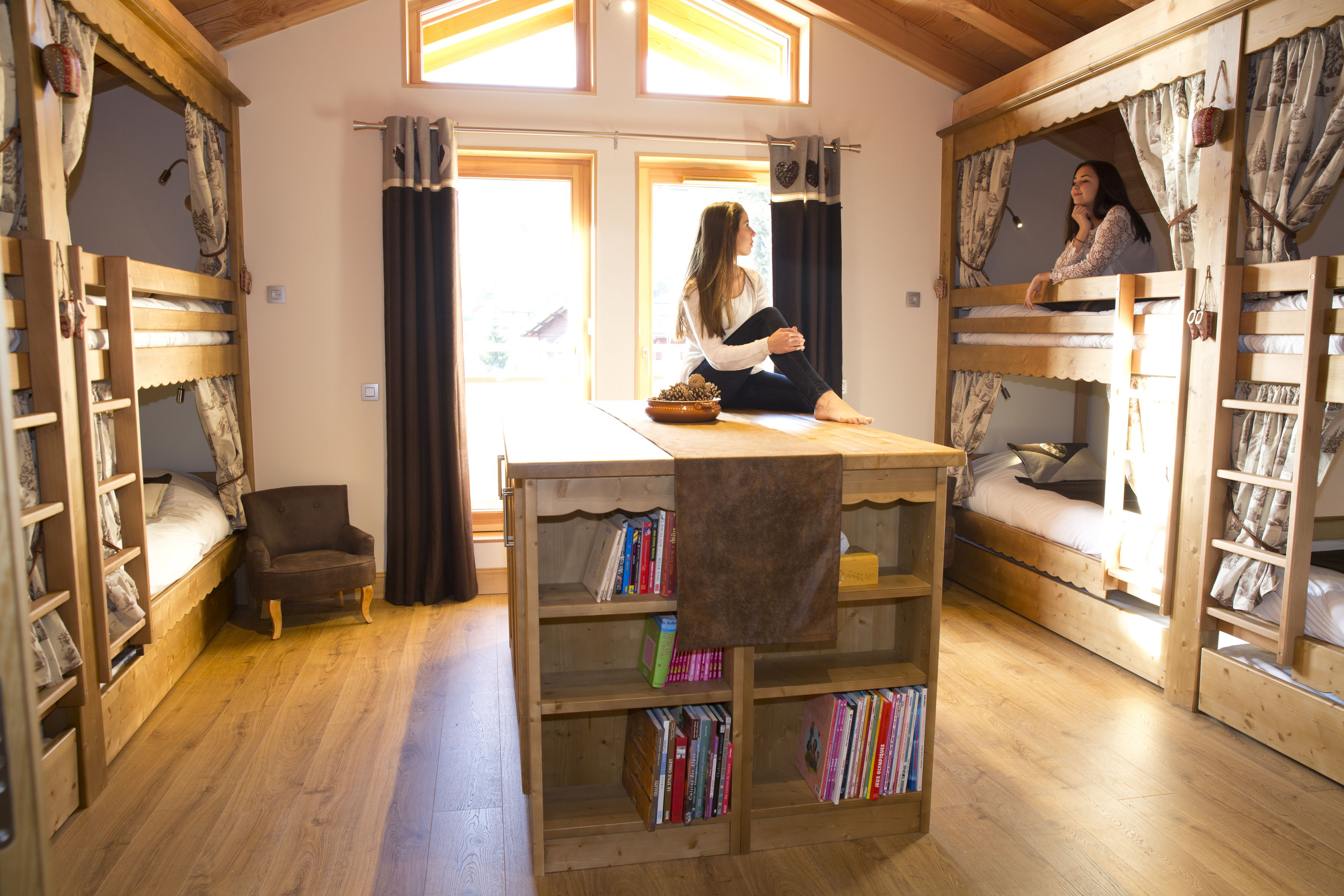 Una habitación acogedora con literas, una pequeña mesa con libros y una silla.