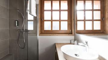 Un baño con ducha, lavamanos y ventana con vidrios satinados.