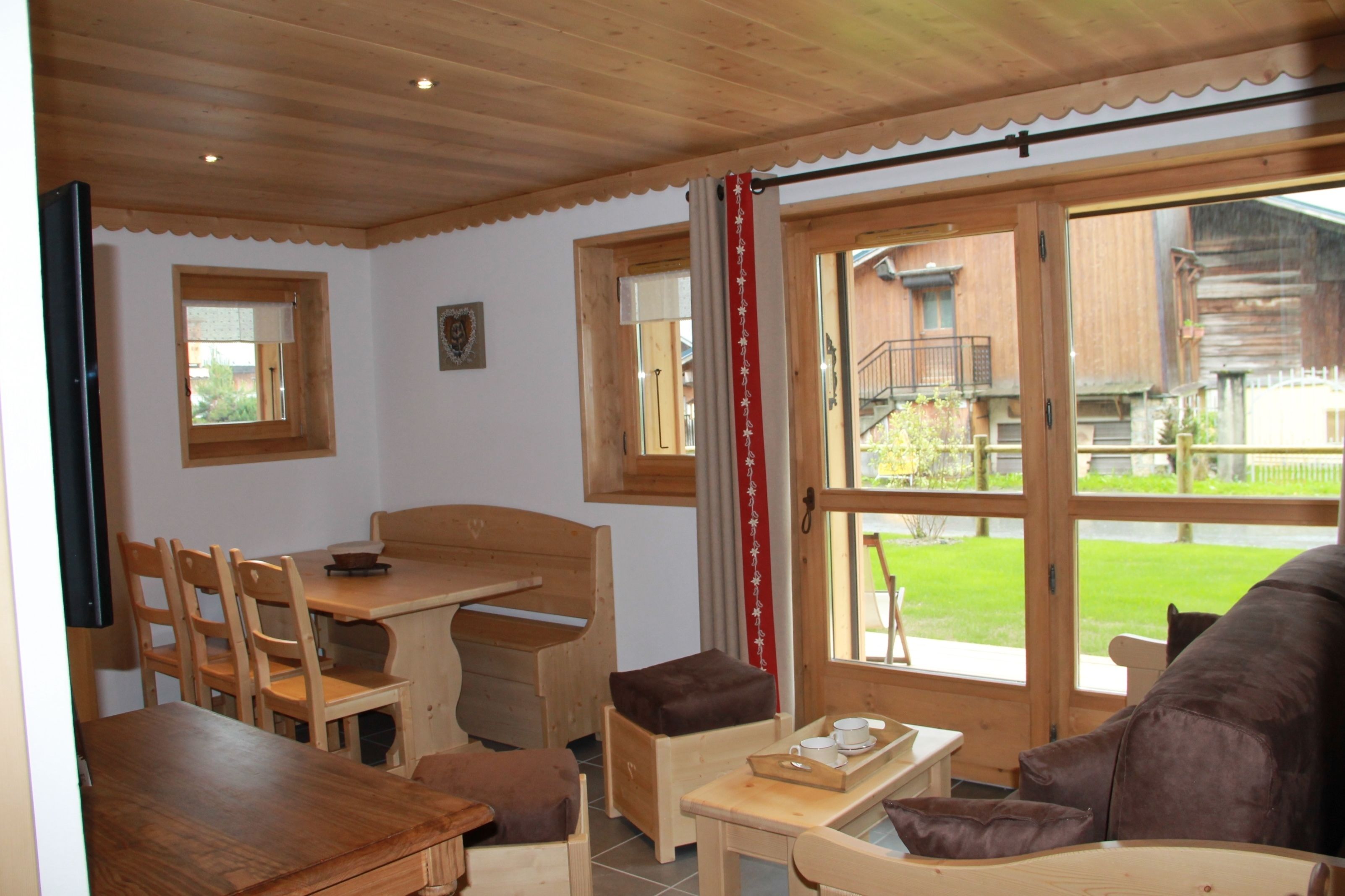 Un interior de madera con una mesa de comedor, sillas, un sofá y un ventanal con vistas al exterior.