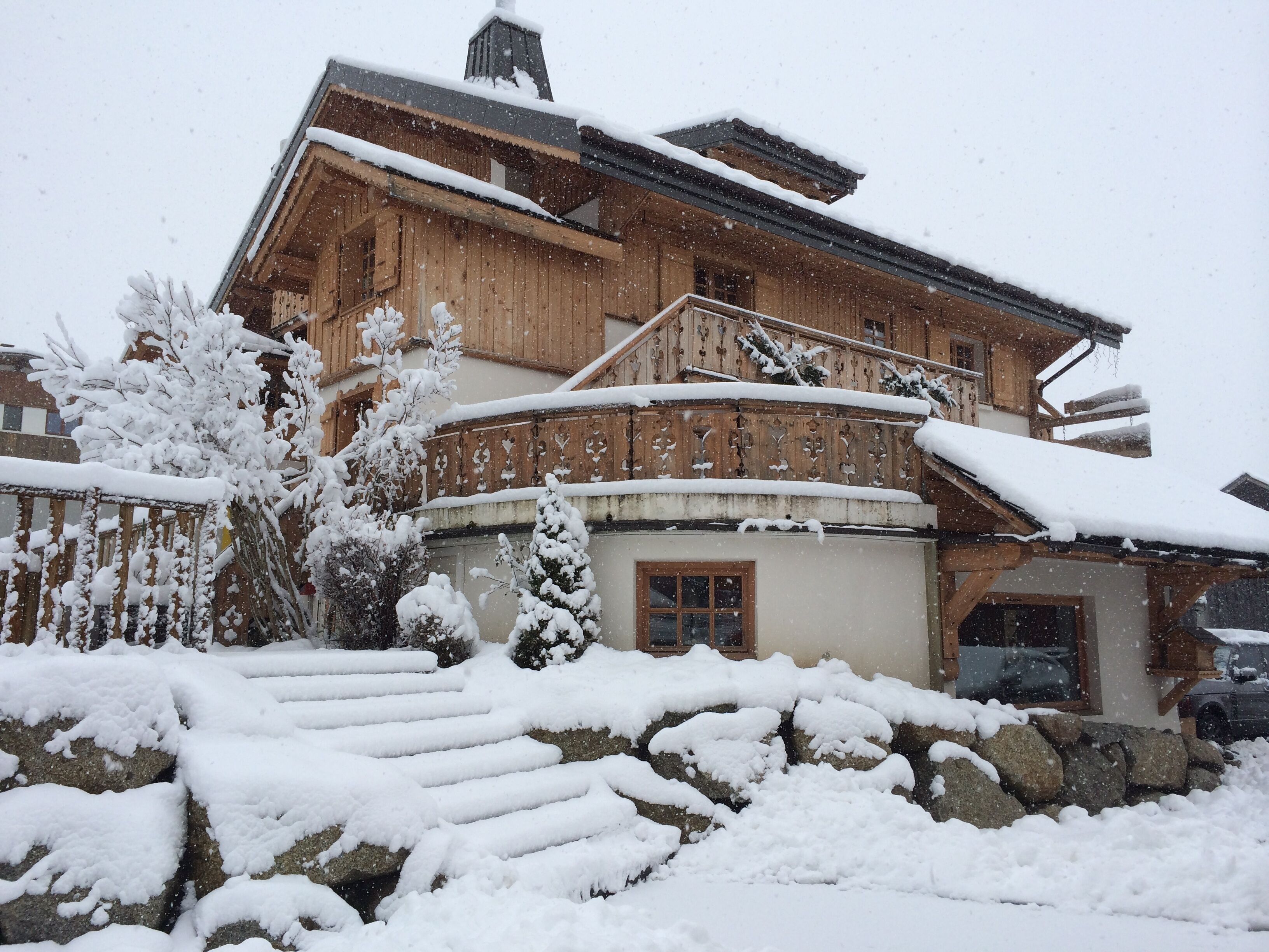 A wooden chalet with a stone foundation, wooden balconies, and a snow-covered landscape.