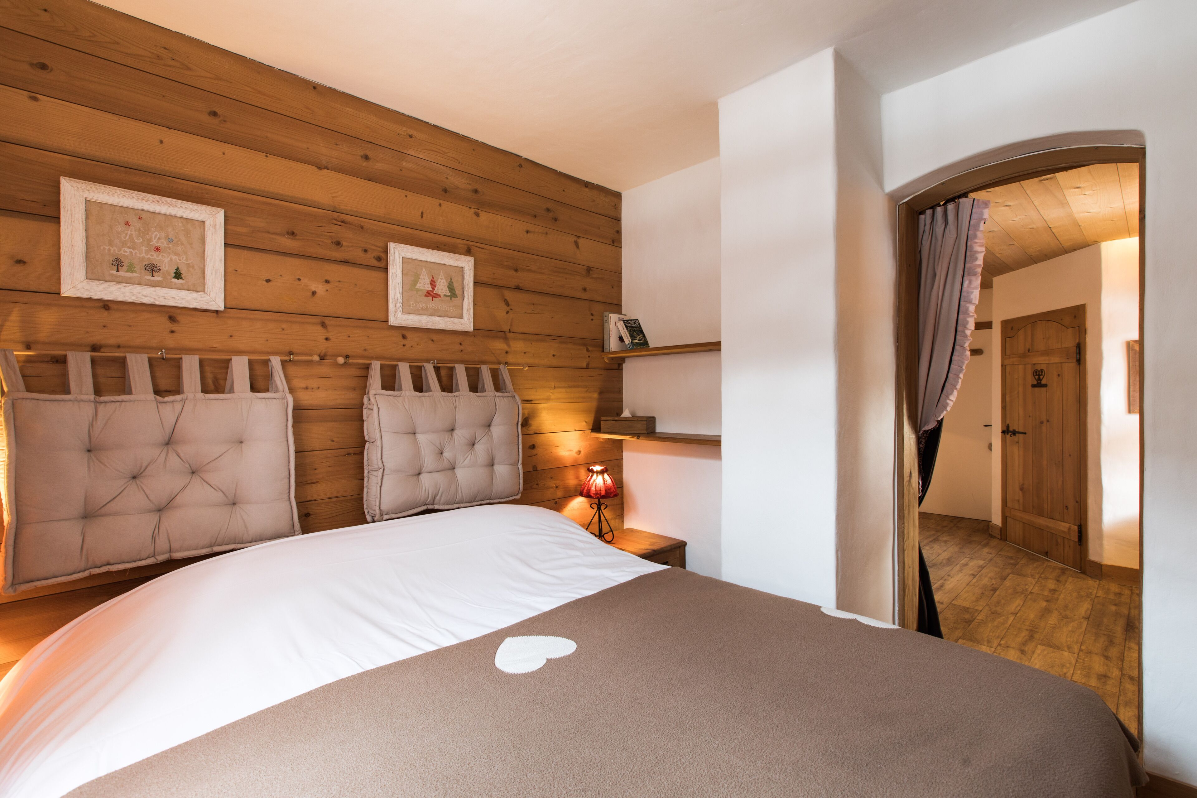 A bedroom with a wooden headboard, a bedside table with a lamp, and a door leading to another room.