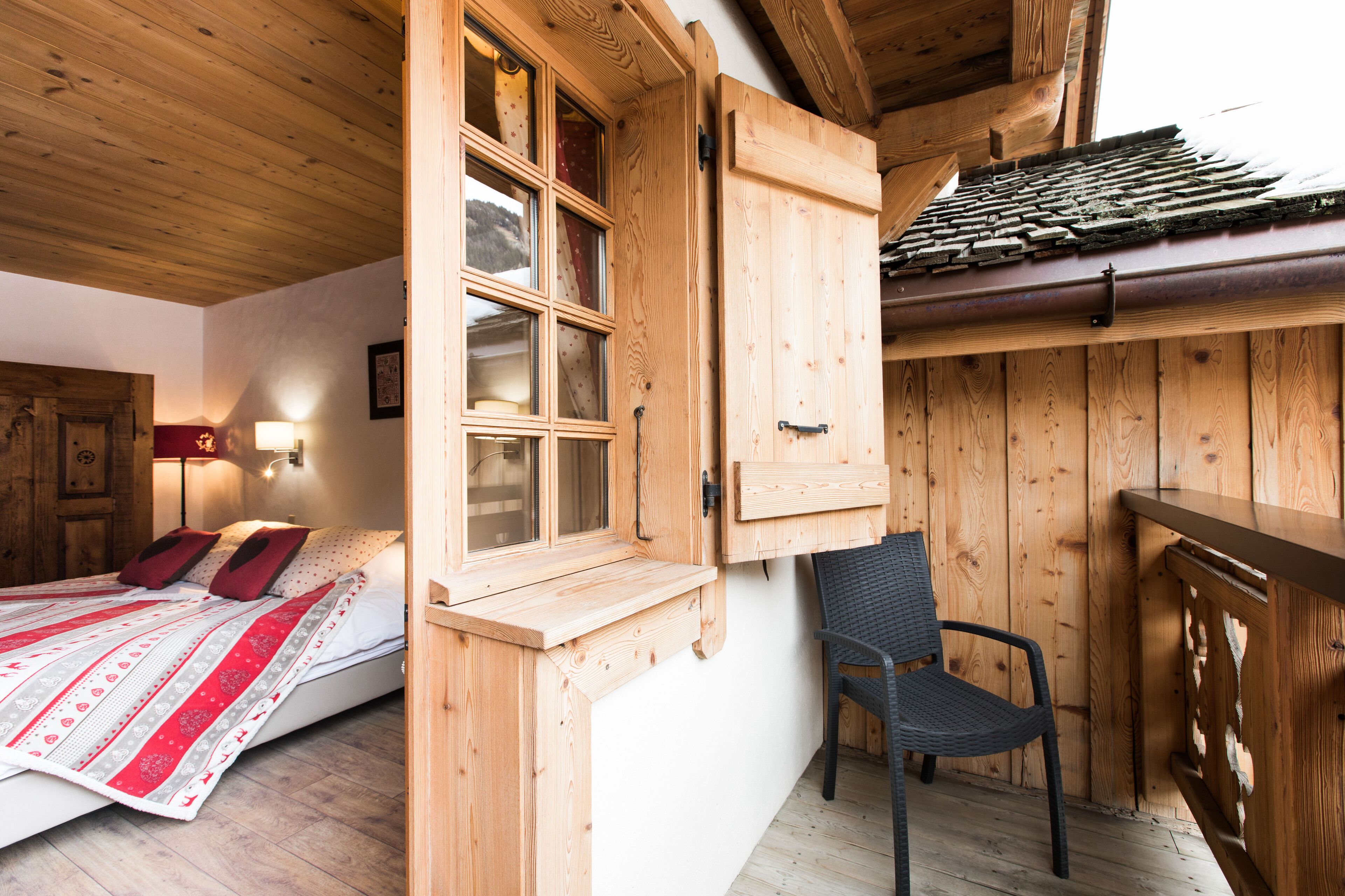 Una camera in una casetta di legno, con un letto, una sedia e una finestra con persiana di legno.