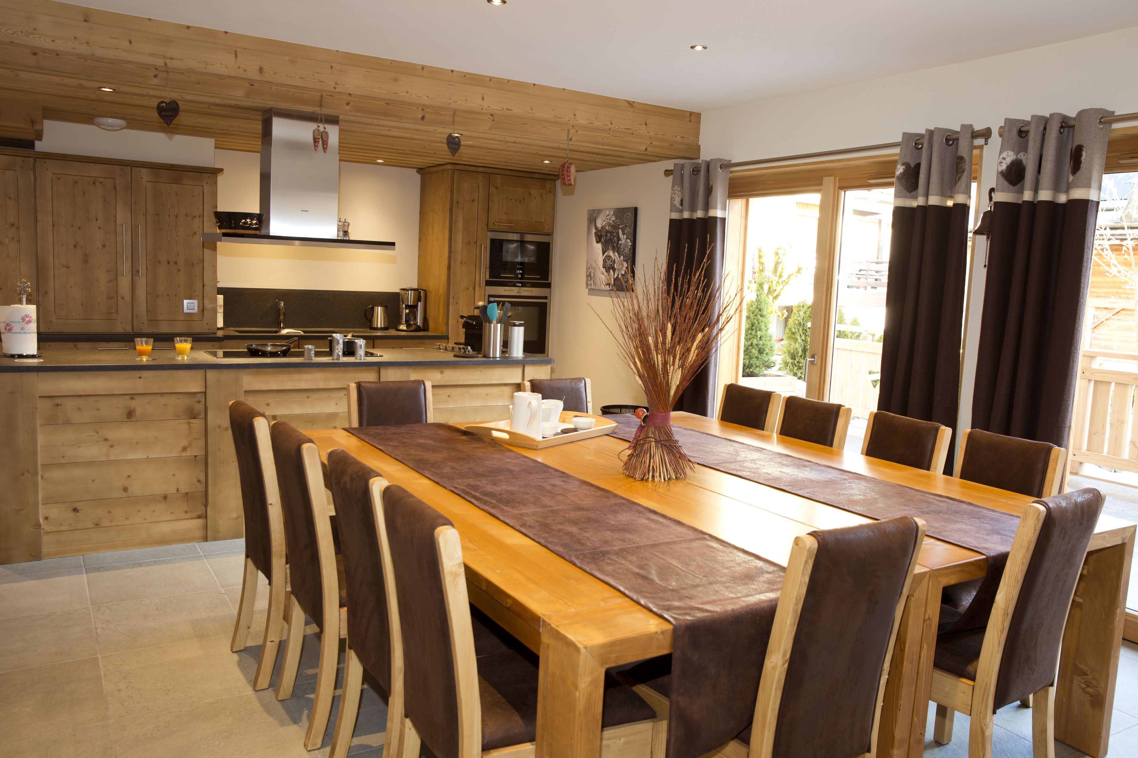 A modern kitchen with wooden cabinets, a central island, and a dining area with a long table and chairs.