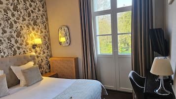 Ein Hotelzimmer mit Bett, Schreibtisch, Stuhl, Lampe, Spiegel und einem fenster mit Vorhängen.