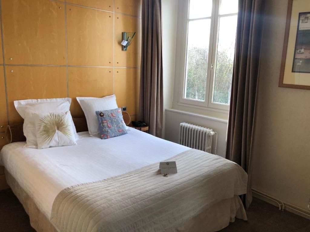 Habitación de hotel con una cama grande, una mesita de noche y un radiador. Cuenta con cortinas en la ventana.
