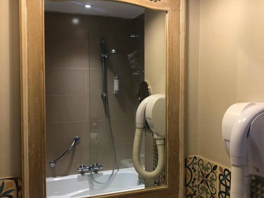 A bathroom with a large mirror, a shower, a toilet, and a hairdryer.