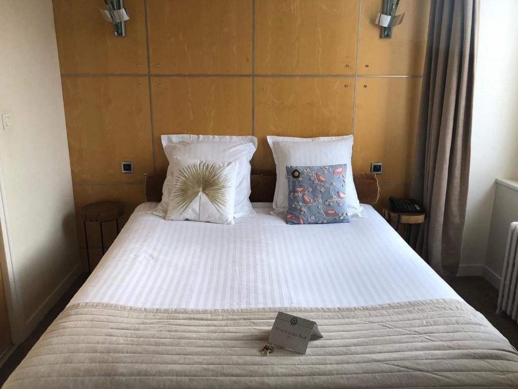 A hotel room with a large bed, two pillows, a bedside table, and a nightstand.