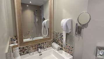 A bathroom with a large mirror, a sink, a towel dispenser, and a handheld mirror.