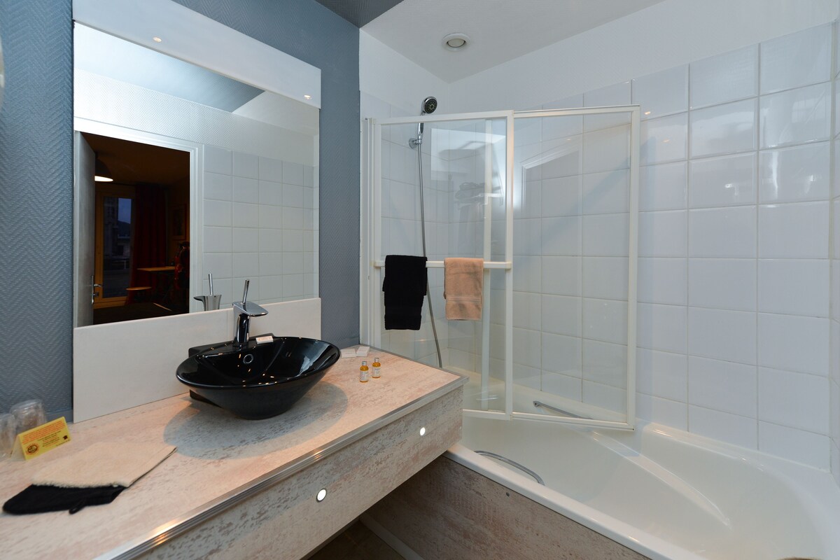 A modern bathroom with a glass-enclosed shower, a large mirror, and a beige countertop with a black vessel sink.