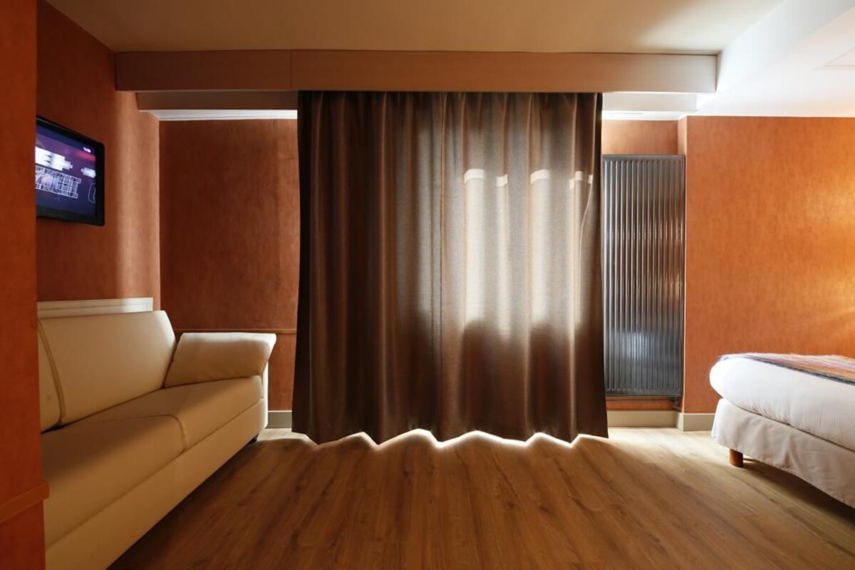 A room with a sofa, a bed, a curtain, and a radiator.