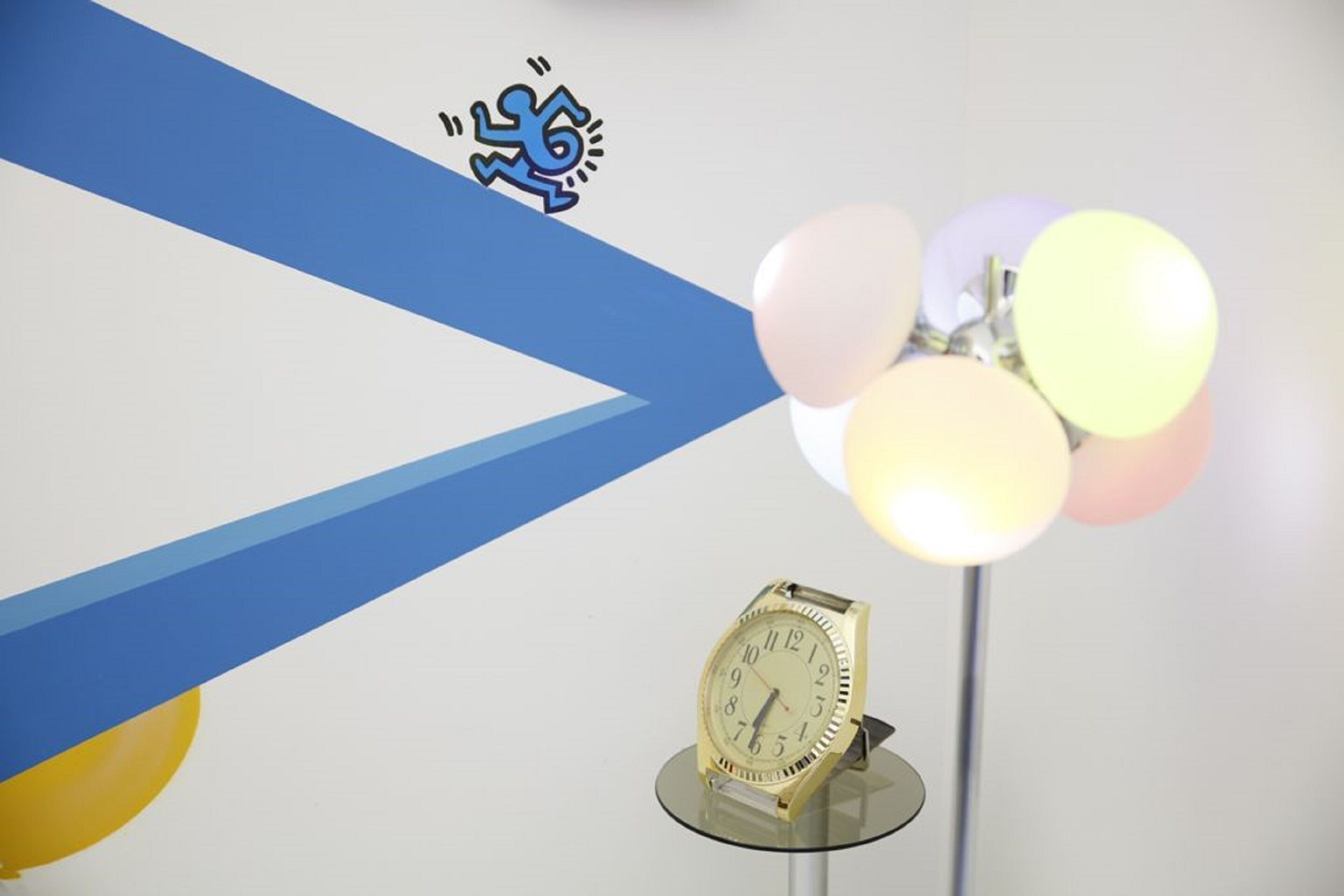 A gold wristwatch on a stand with a blue and white background.