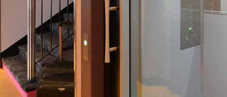 An elevator with a glass door, a control panel, and a suitcase on the floor.