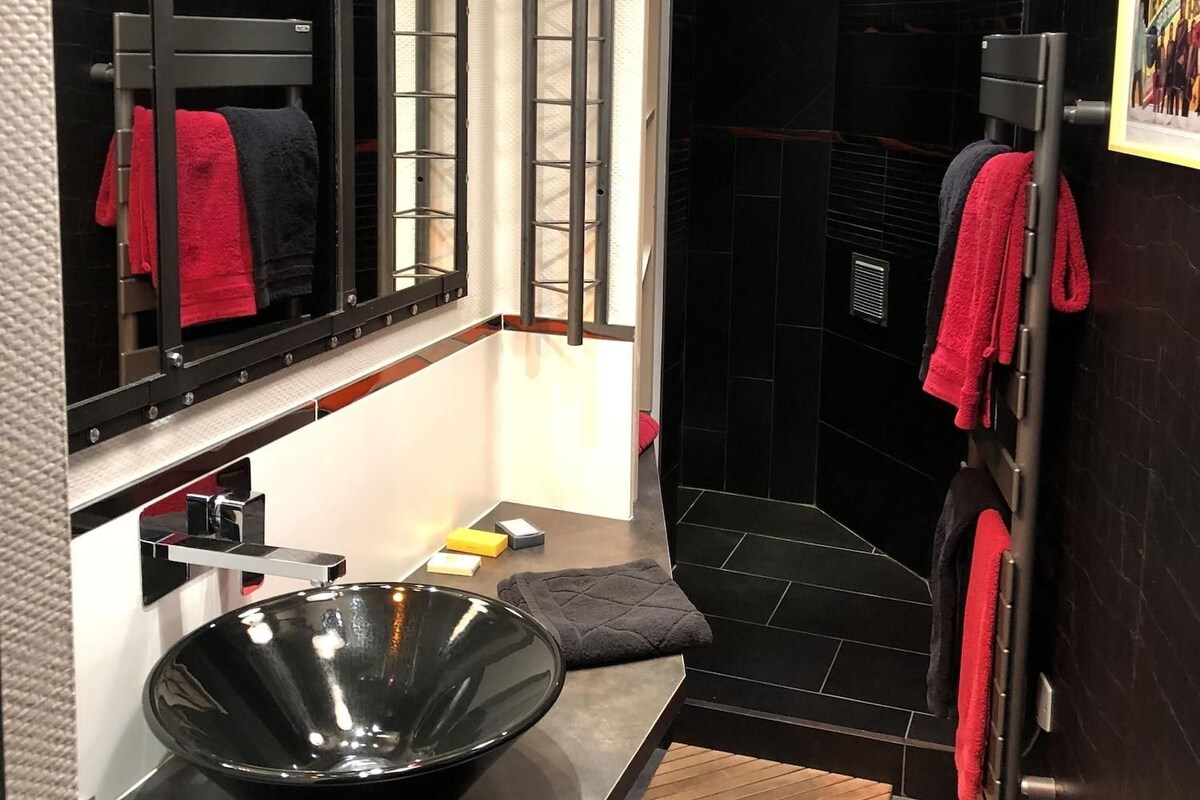 A modern bathroom with a black sink, a large mirror, and a shower area.