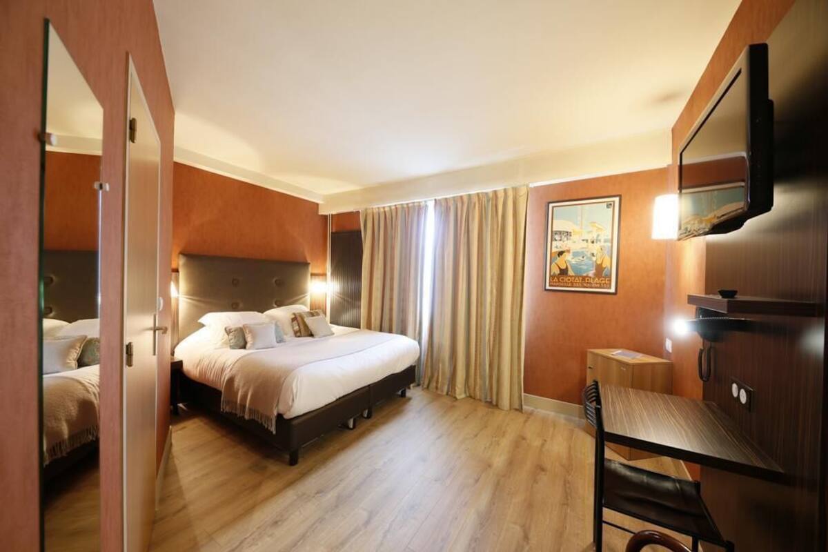 A hotel room with a bed, a desk, a chair, a TV, and a painting on the wall.