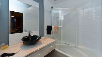 A modern bathroom with a large mirror, a black vessel sink, a glass-enclosed shower, and a beige countertop.