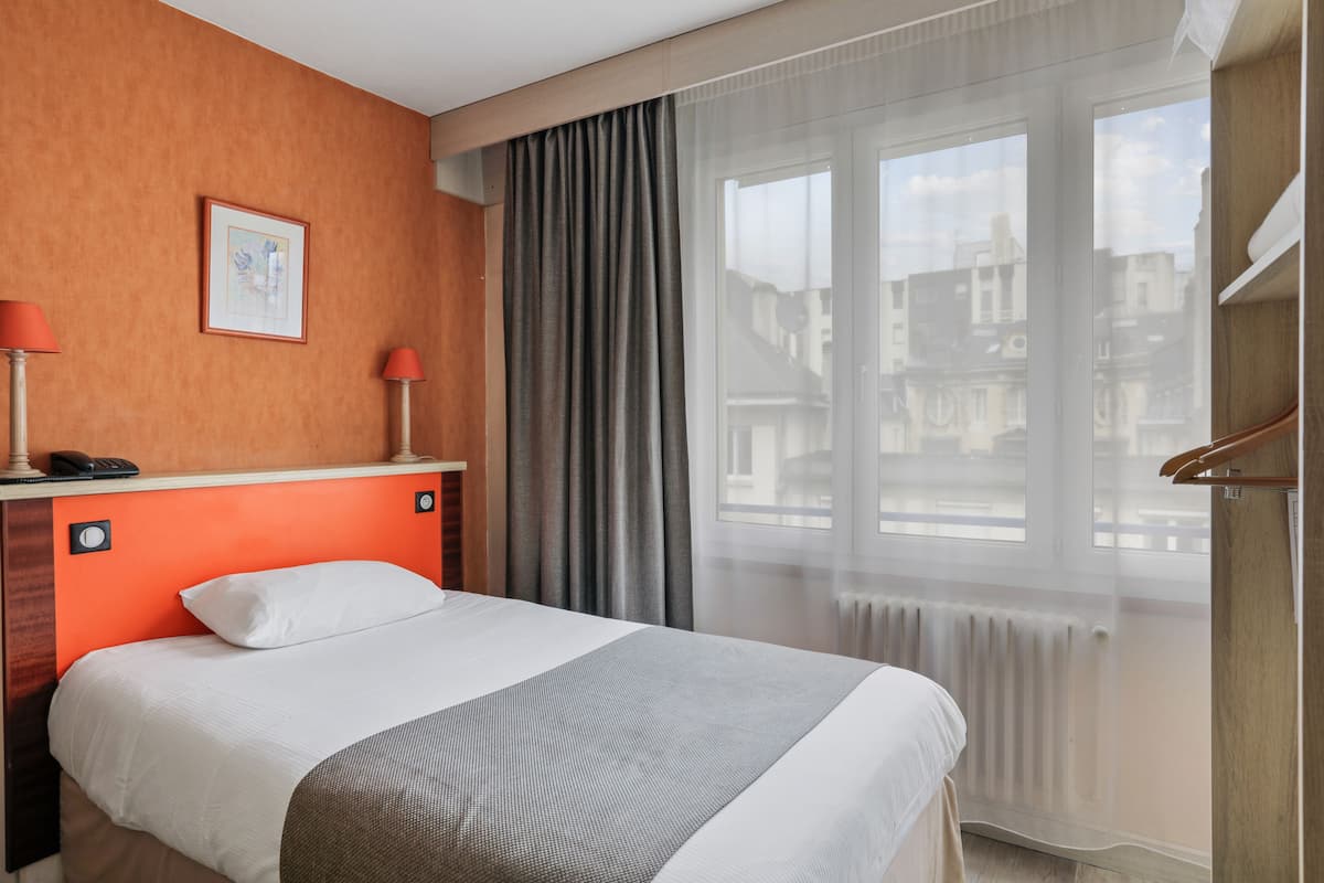 A hotel room with a bed, a desk with a telephone, and a window with curtains.
