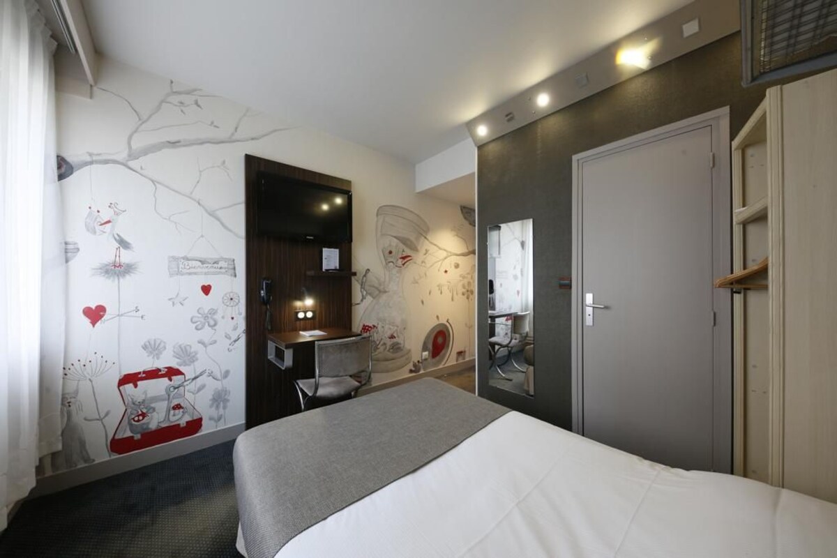 A hotel room with a bed, a desk, a chair, a mirror, and a door.