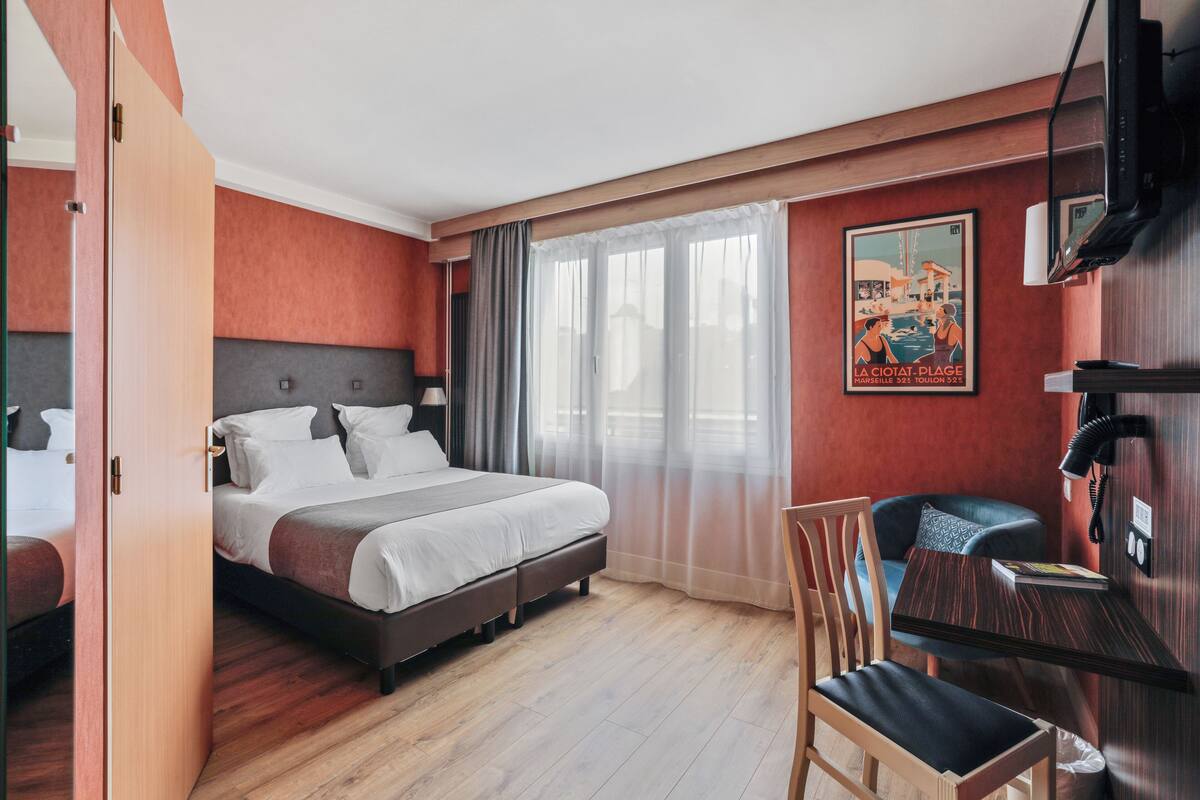 A hotel room with a bed, a desk, a chair, a television, and a poster on the wall.