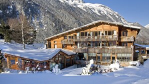 A wooden chalet with multiple balconies, surrounded by snow-covered mountains.