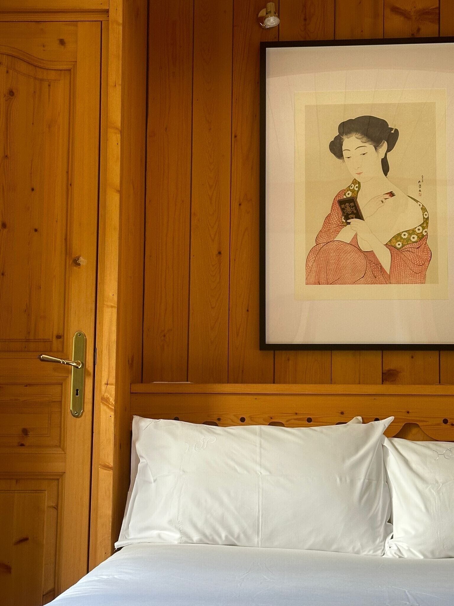 A wooden-paneled room with a bed, a framed picture on the wall, and a door with a key lock.