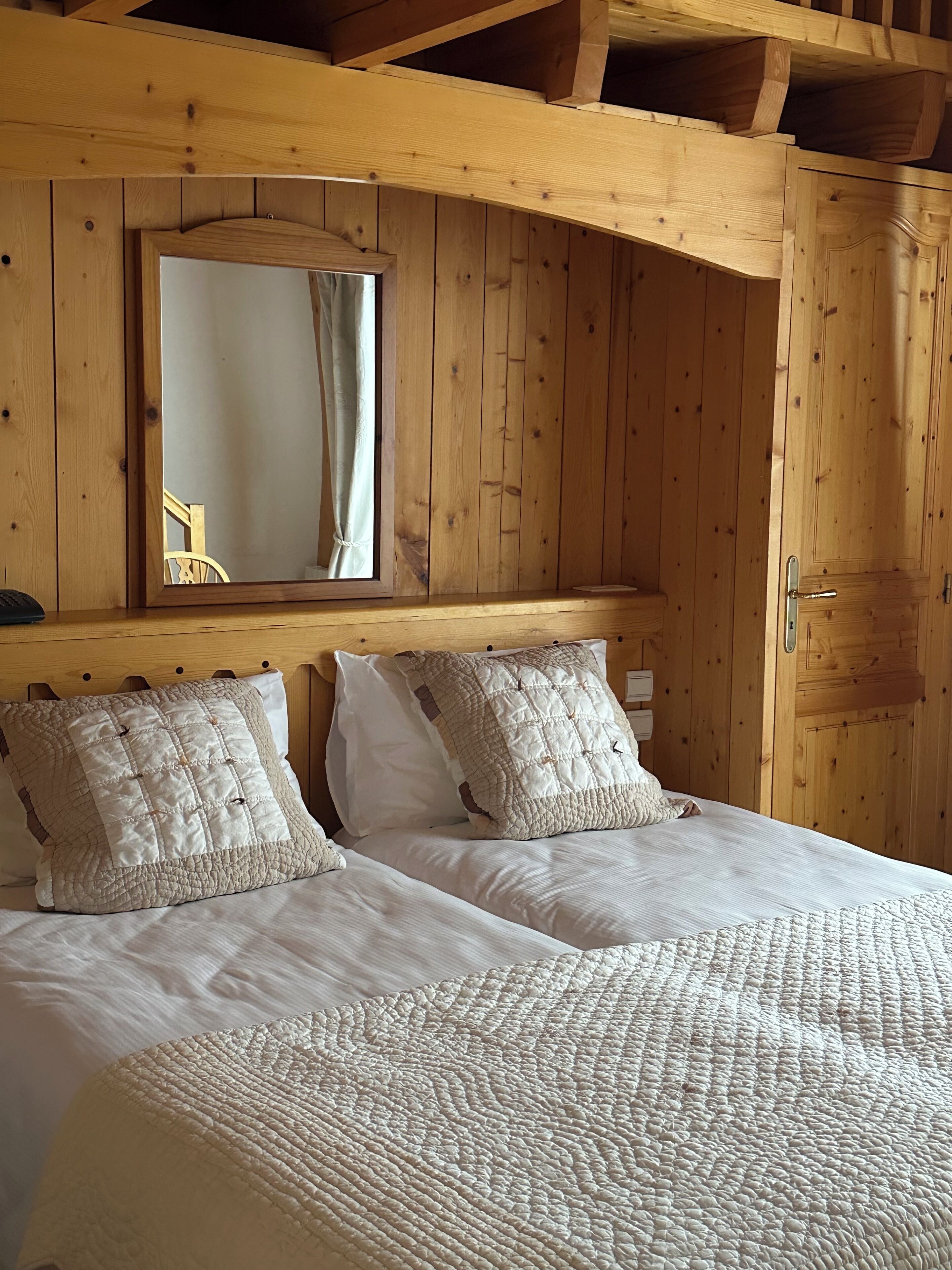 Una habitación de cabaña de madera con una cama, dos almohadas, un espejo y una puerta de madera.