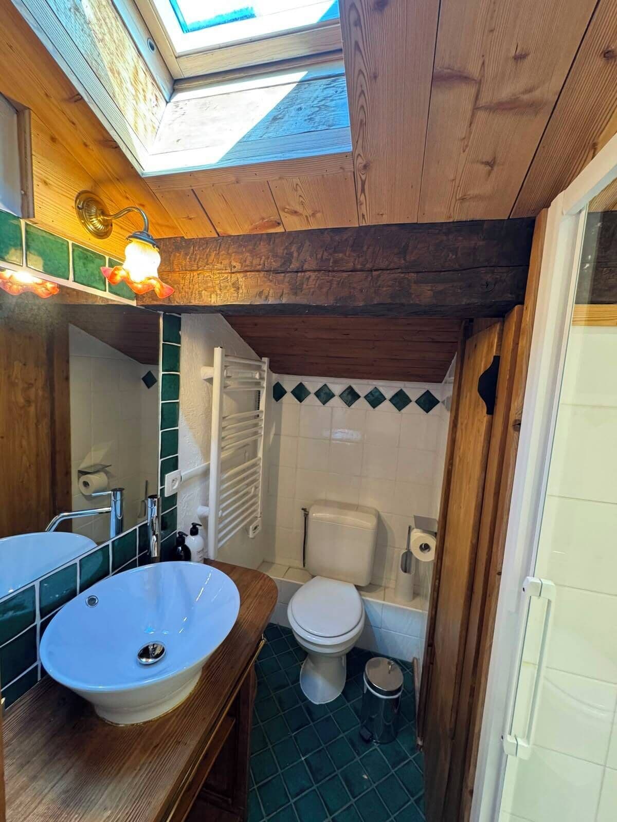 Casa de banho compacta com claraboia, toucador de madeira, lavatório branco, sanita e zona de duche.