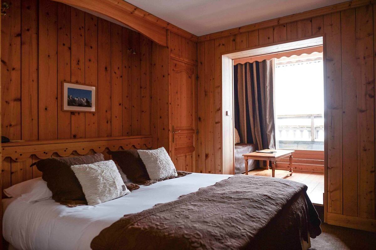 Een houten kamer met een bed, een tafeltje en uitzicht door een raam.