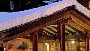 A wooden cabin with a glass-enclosed pool, surrounded by snow.