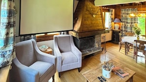 A cozy room with a fireplace, two armchairs, a wooden coffee table, and a projector screen.