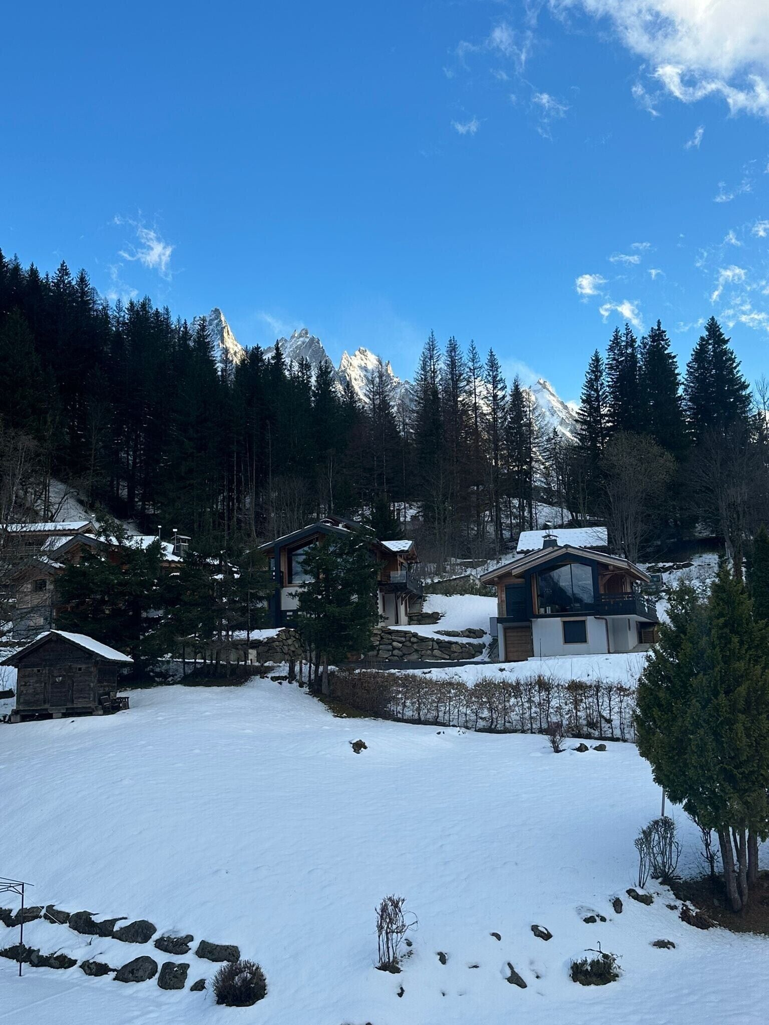 Un paisaje nevado con una montaña al fondo, varias cabañas de madera y un cielo azul despejado.