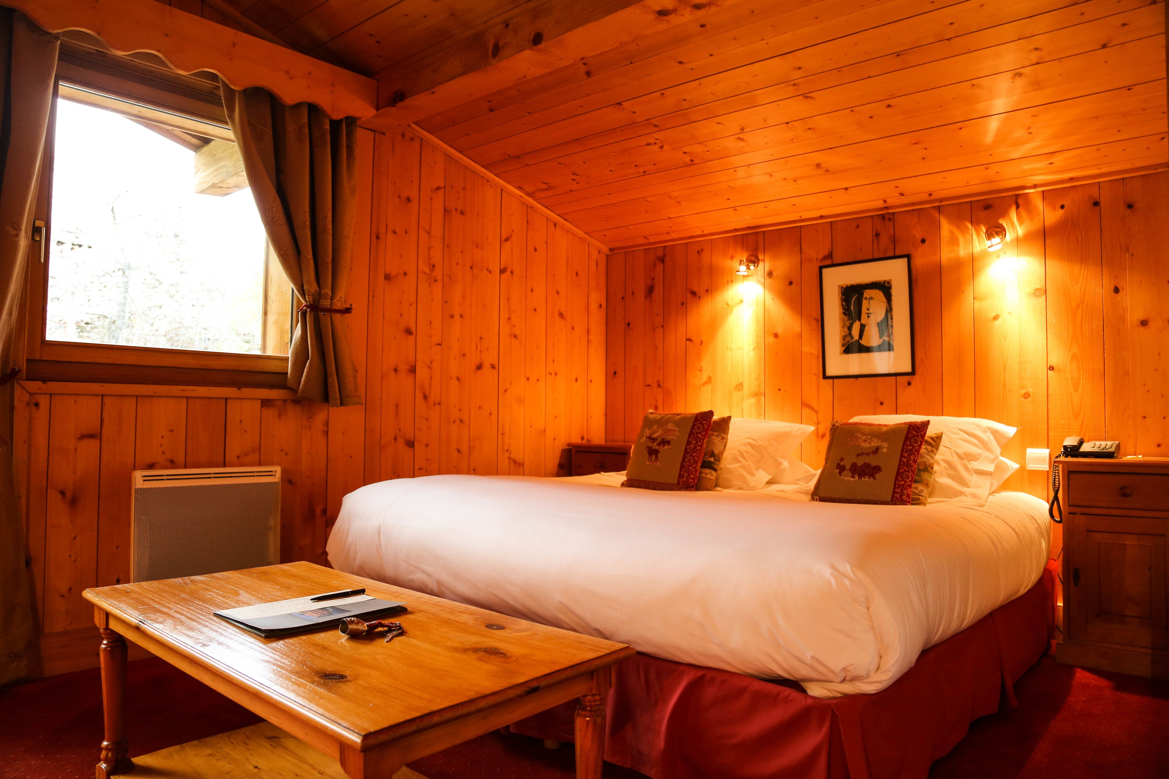 Una habitación tipo cabaña de madera con una cama grande, un escritorio y una ventana con cortinas.