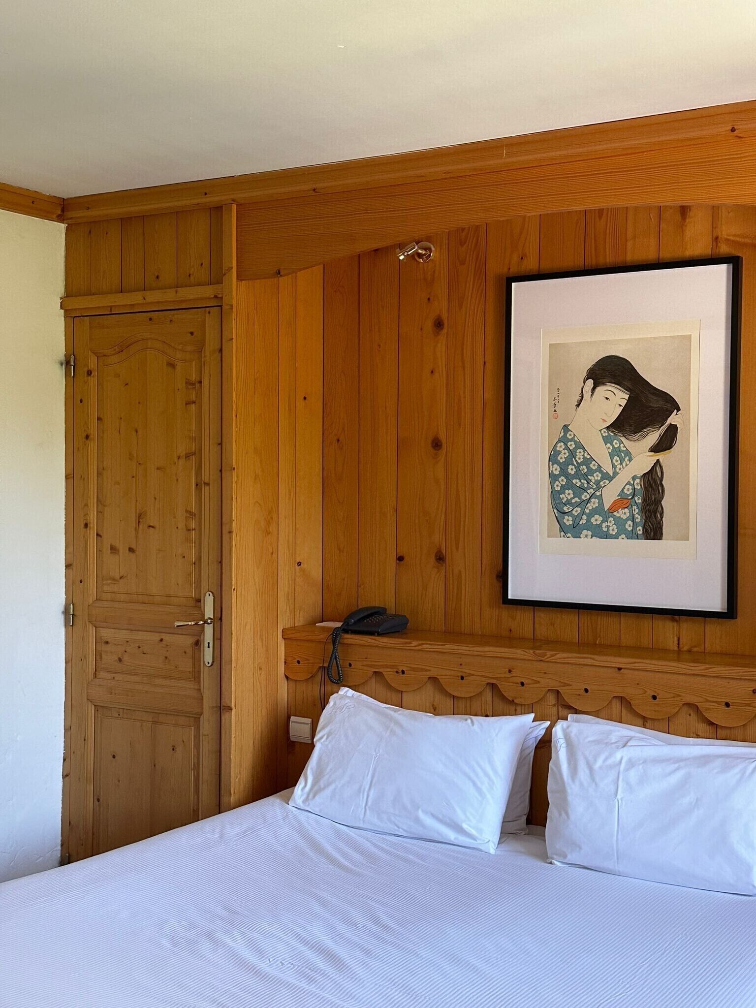 Una habitación con paneles de madera, una cama, un teléfono y un cuadro en la pared.