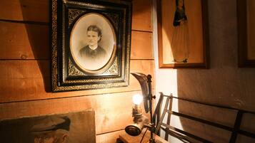 A room with wooden walls, a framed portrait, a vintage desk lamp, and a painting.