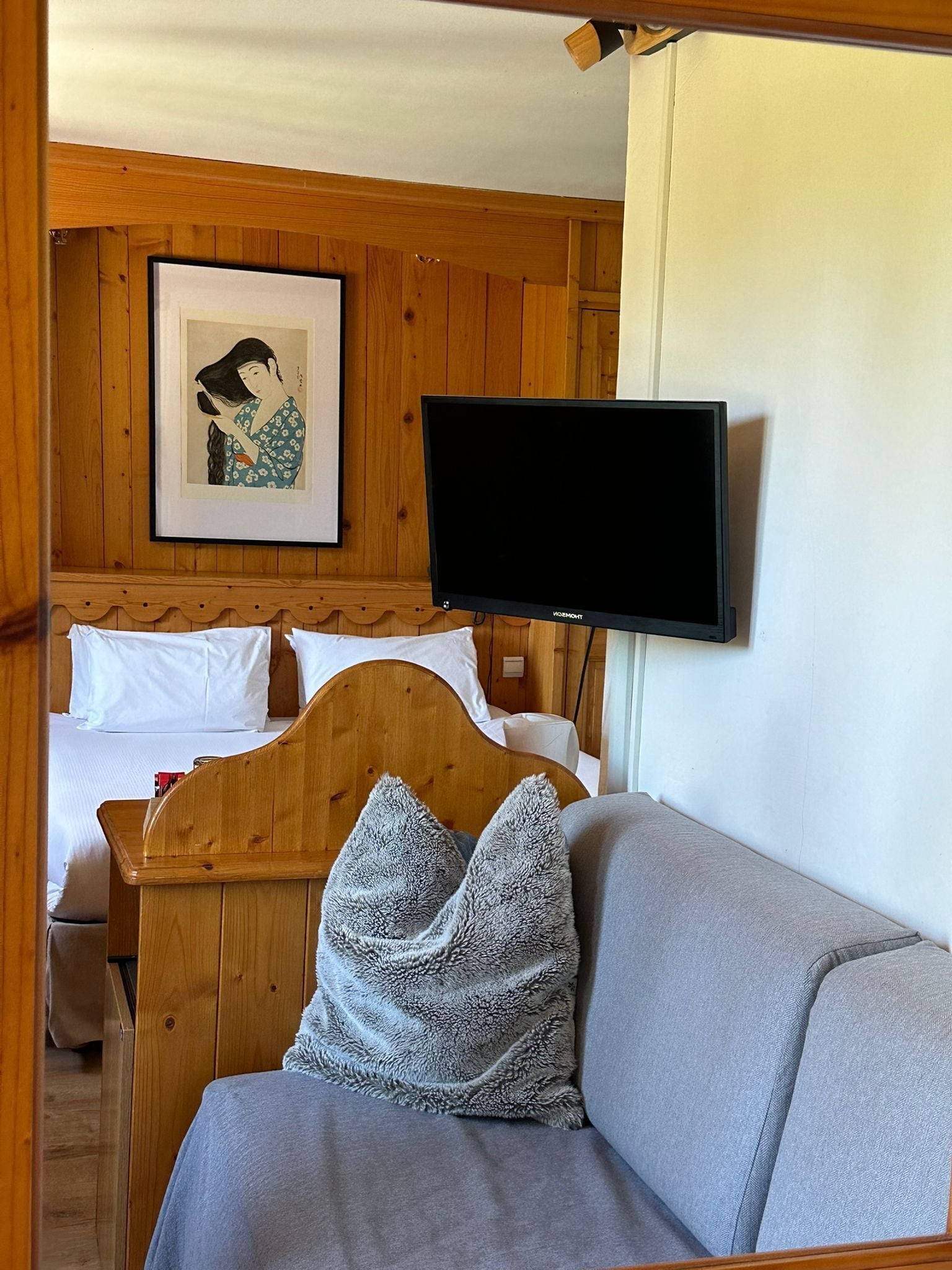 A wooden room with a bed, a television mounted on the wall, and a framed artwork above the bed.