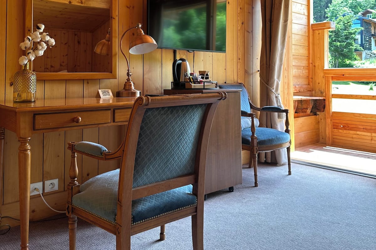 Een kamer met houten lambrisering, een bureau, stoel, televisie en een raam met uitzicht op groen.
