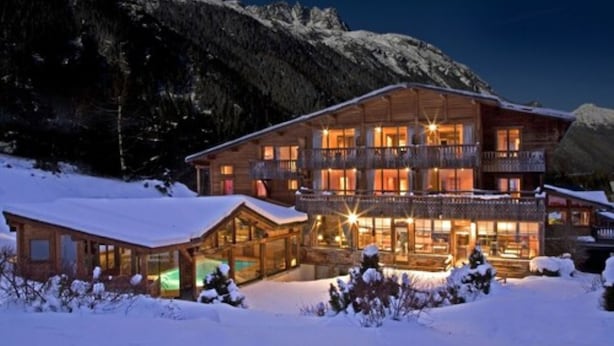 A large, multi-story wooden lodge with balconies, surrounded by snow-covered mountains.