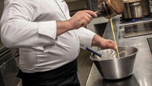 A chef in a professional kitchen, pouring a liquid from a pot into a bowl. - Le Beau Rivage (Condrieu)