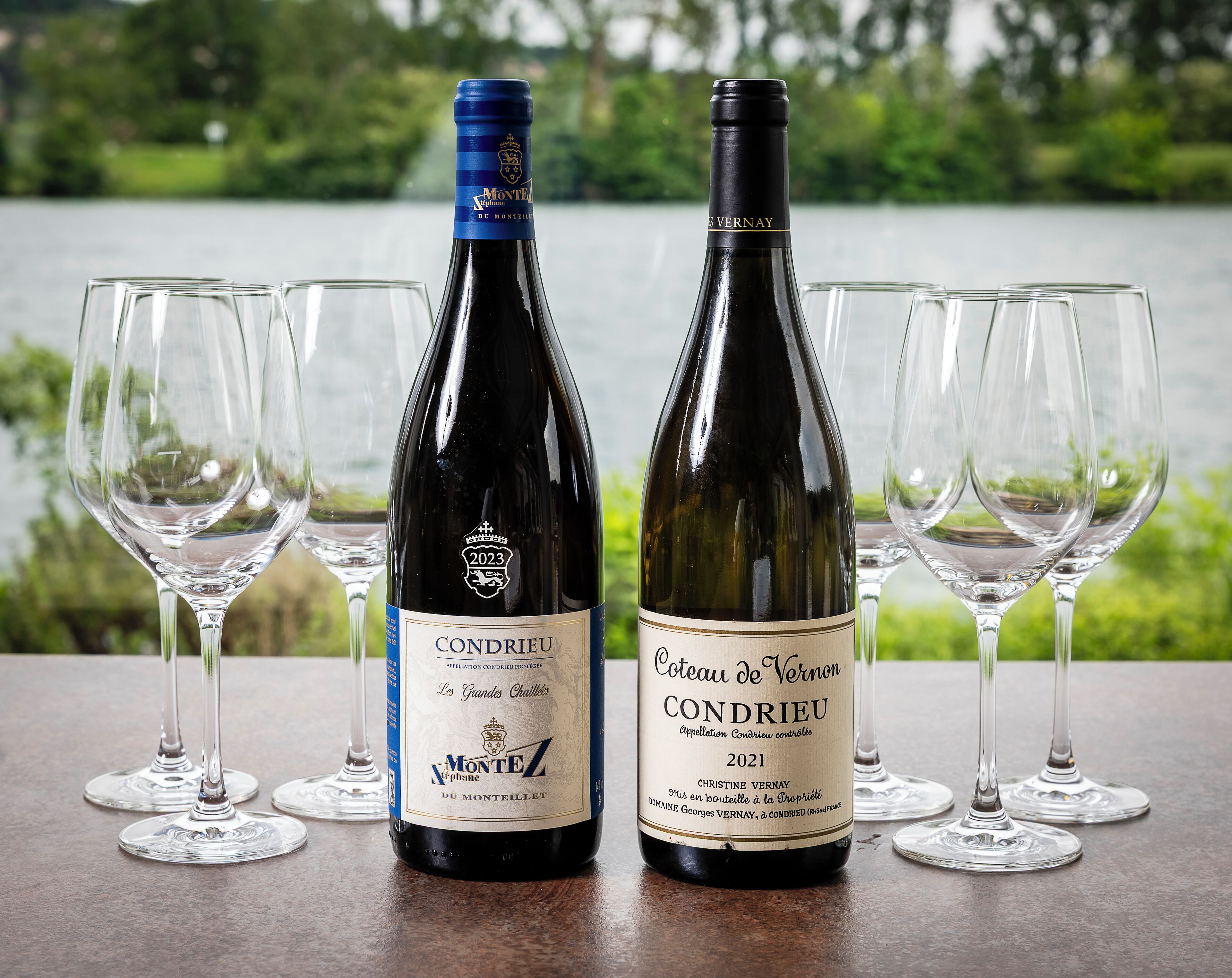 Two bottles of wine, one labeled 'Montez' and the other 'Coteau de Vernon', with empty wine glasses arranged around them.