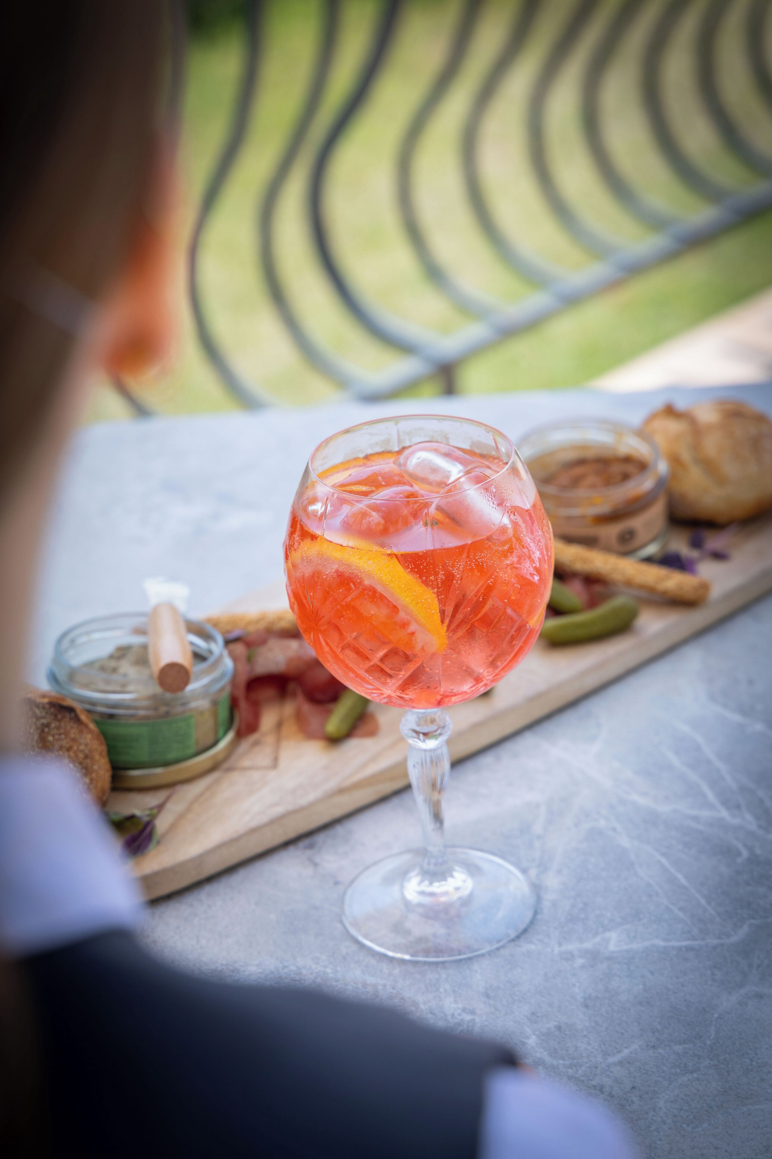 A glass of red beverage with an orange slice, a jar of spice, and a baguette on a wooden board.